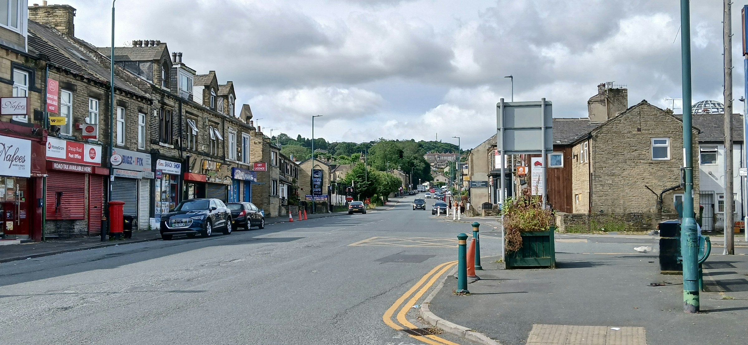 Stone terraced houses, corner shops and a post box along a street of stone terraces