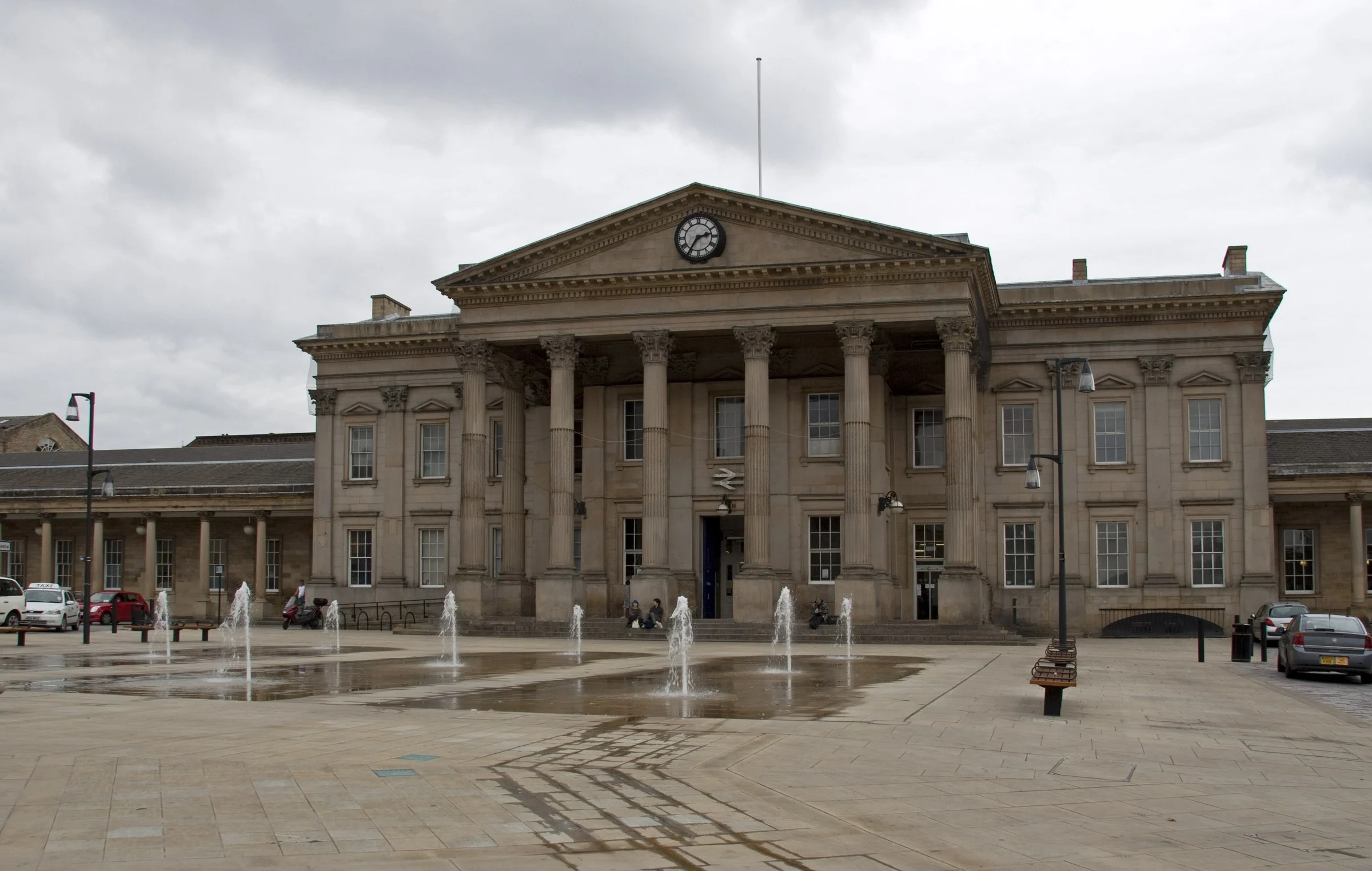 Corinthian portico and clock of Huddersfield railway station across St George's Square, with fountains