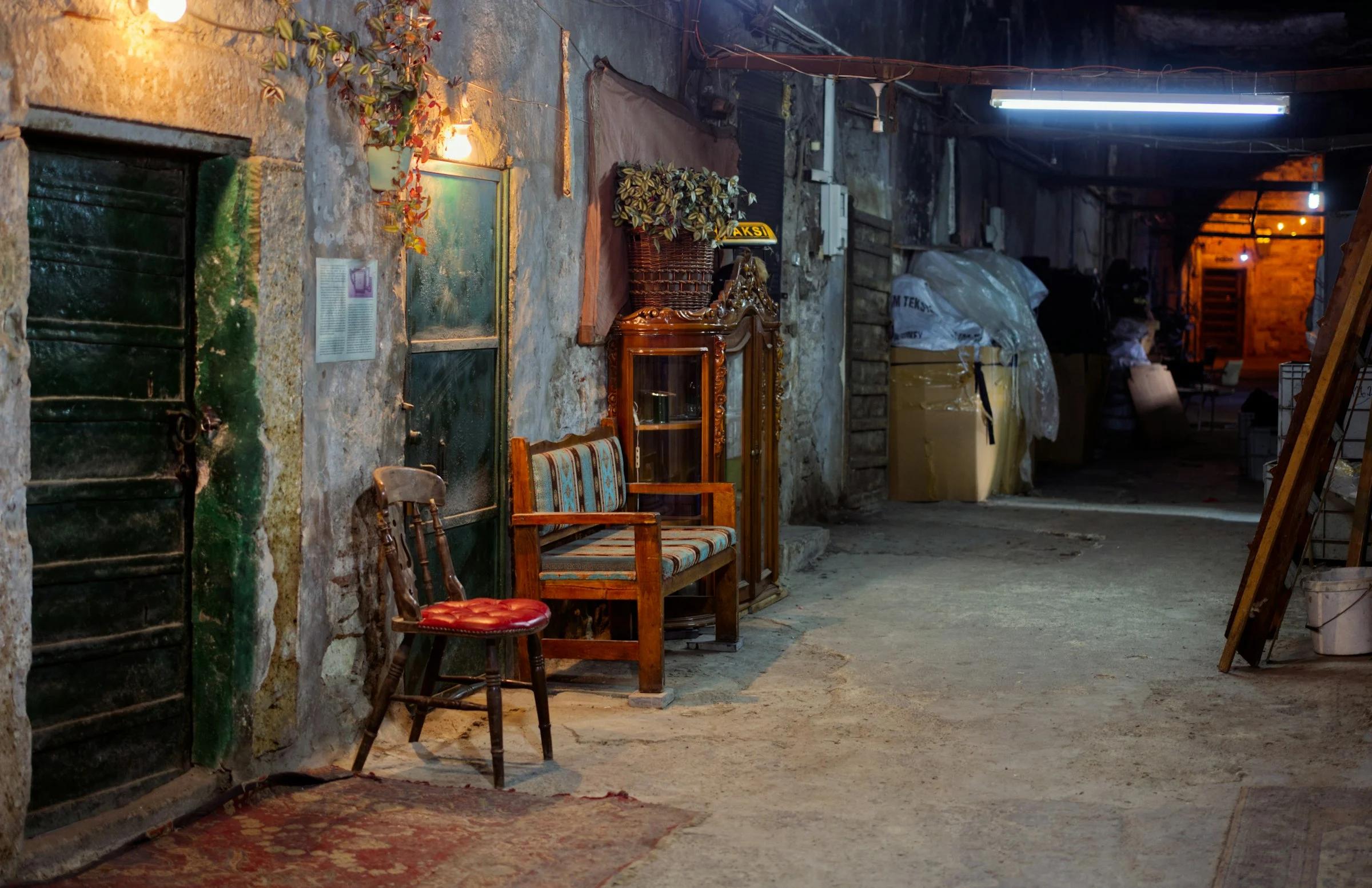 Dim stone store passage with a Windsor chair, a bench, a glazed cabinet and furniture wrapped in plastic