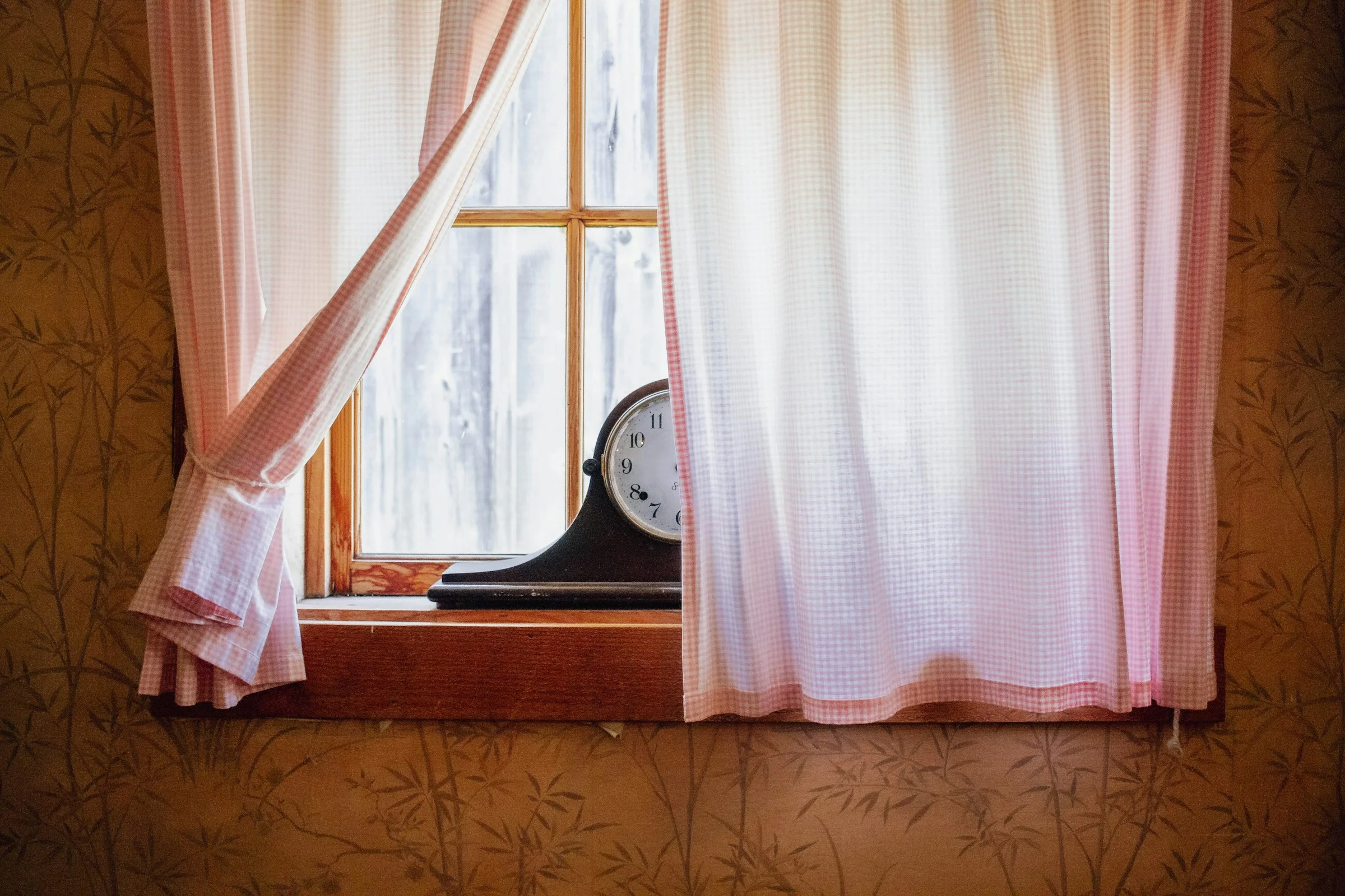 Tambour mantel clock on a windowsill between pink gingham curtains