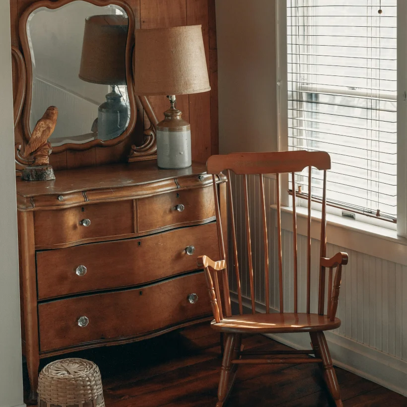 A chest of drawers and a rocking chair in a sunlit bedroom