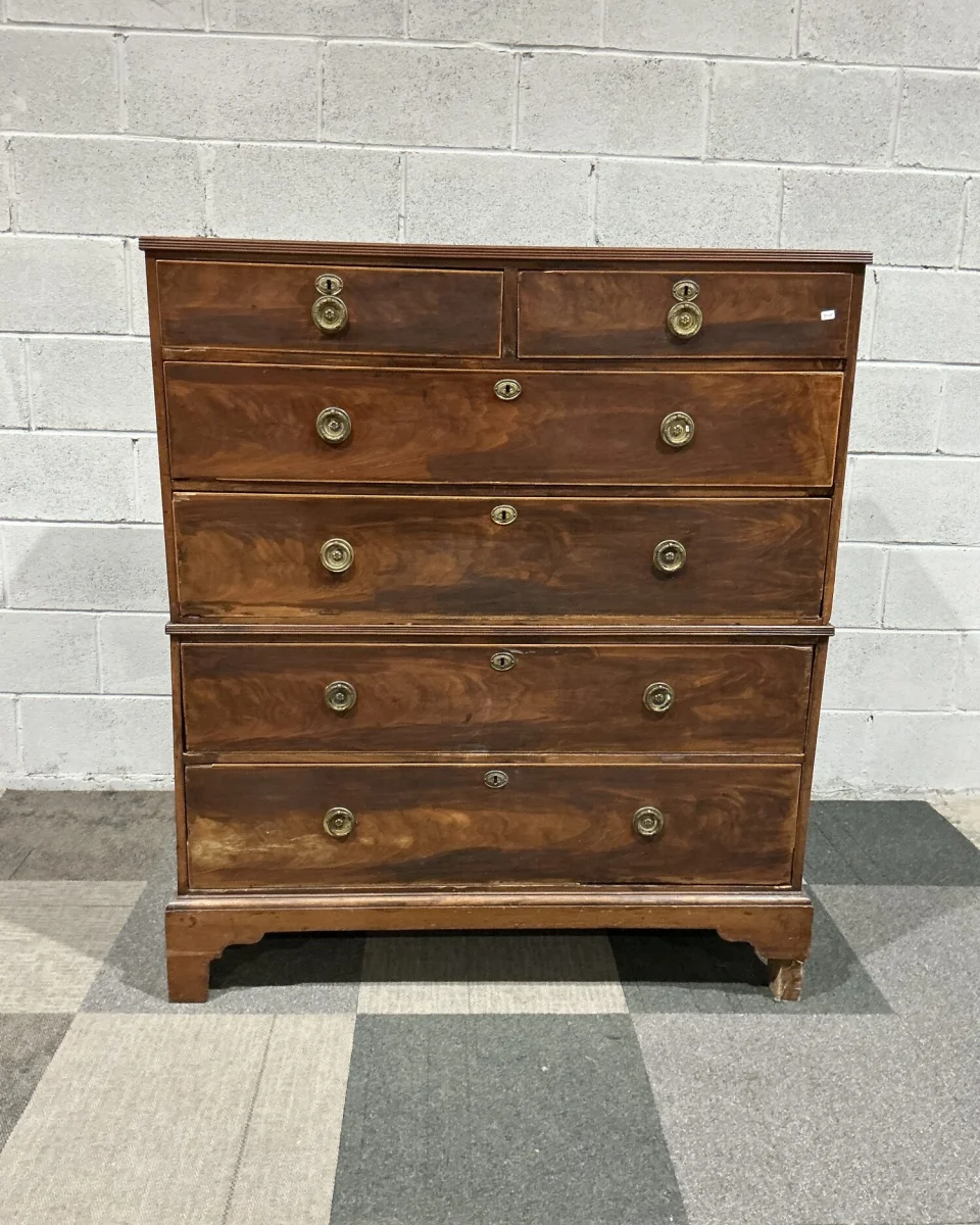 A George III flame mahogany chest-on-chest standing against the breeze-block wall of our premises