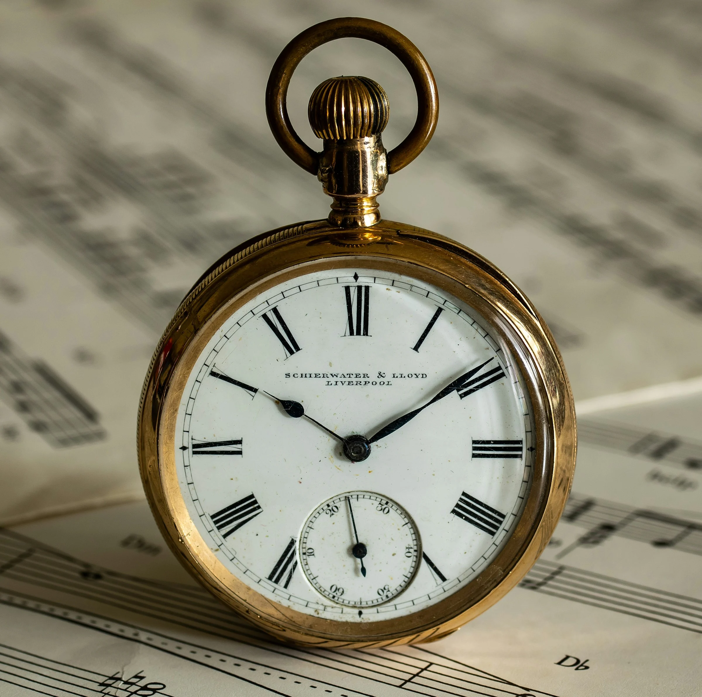 Gold open-face pocket watch with an enamel dial, lying on sheet music