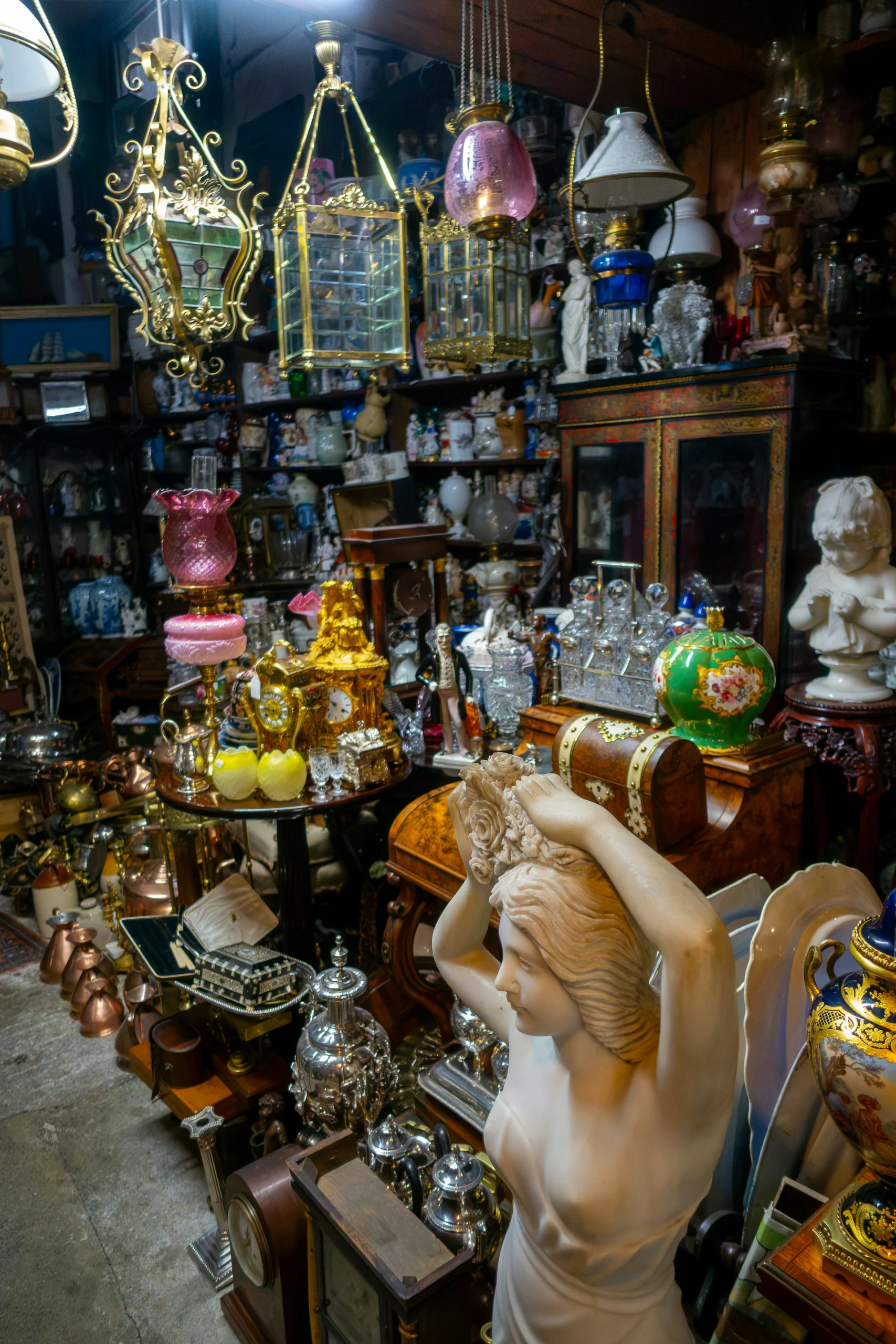 Packed antique shop with brass hall lanterns, cranberry glass oil lamps, ormolu clocks and marble figures