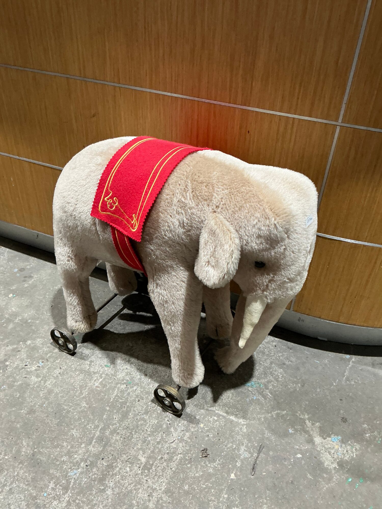 Vintage German pull-along toy elephant on cast wheels, against a wood-panel backdrop